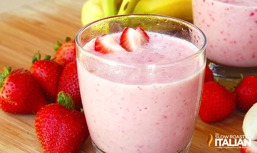 strawberry and banana smoothie in a glass surrounded by fresh strawberries