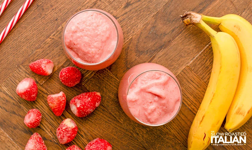 overhead: two full glasses of strawberry banana smoothie surrounded by fruit
