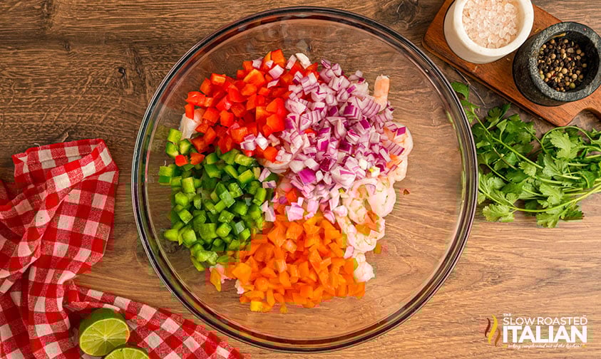 adding vegetables to the cooked shrimp in a large mixing bowl