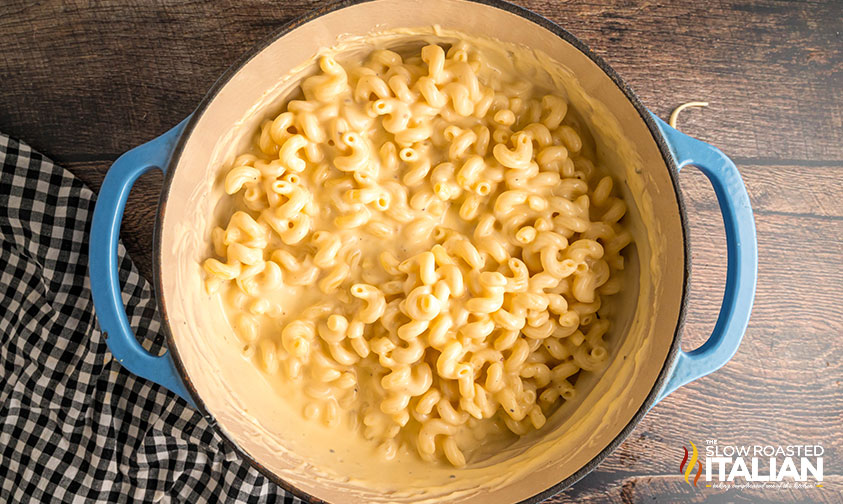 adding cooked pasta to cheese sauce in dutch oven