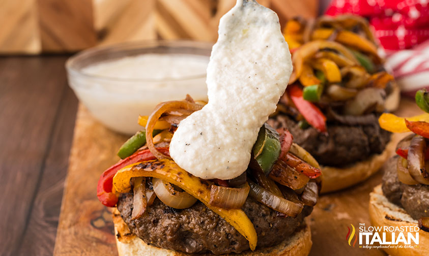 adding smoked provolone sauce to philly cheesesteak burger