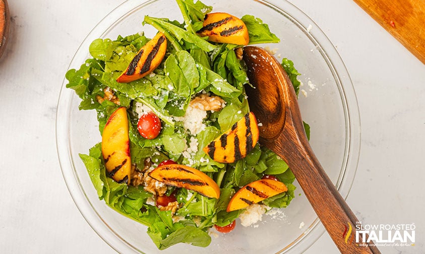adding grilled peaches to salad in a mixing bowl