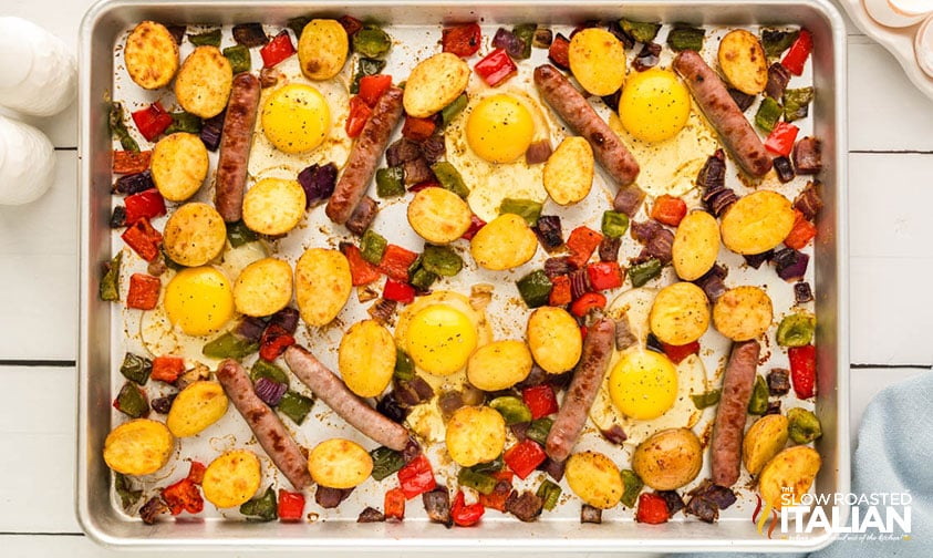 cracking eggs onto sheet pan with sausage and veggies