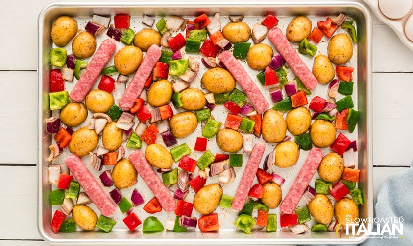 adding sausage links to sheet pan full of veggies