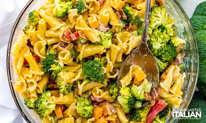 overhead: spoon resting in large bowl of pasta broccoli salad with cheddar cheese and bacon