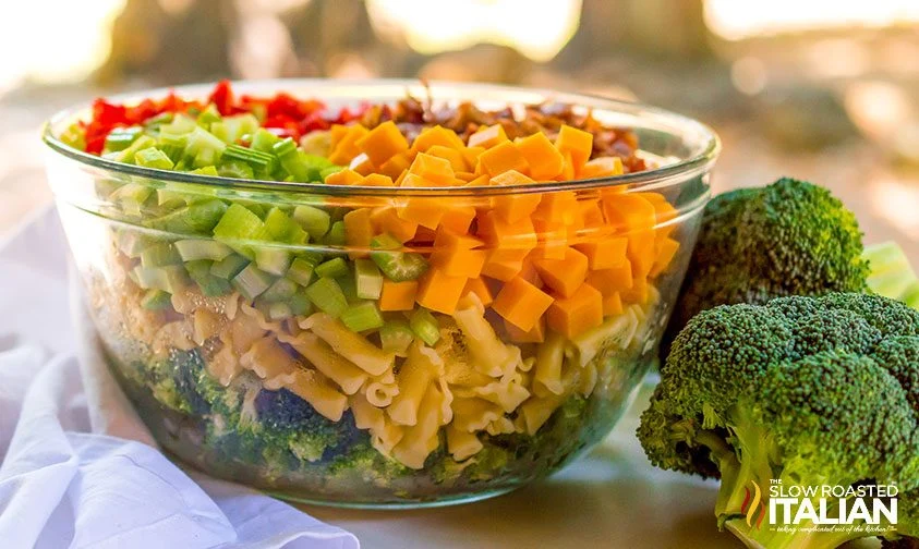 ingredients for broccoli cheddar pasta salad layered in a clear bowl