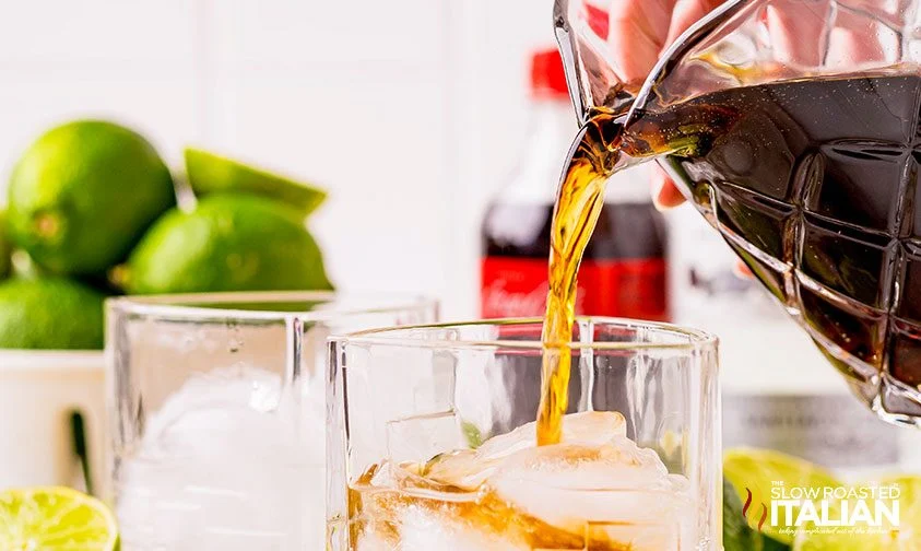 pouring cola into glass with ice and rum