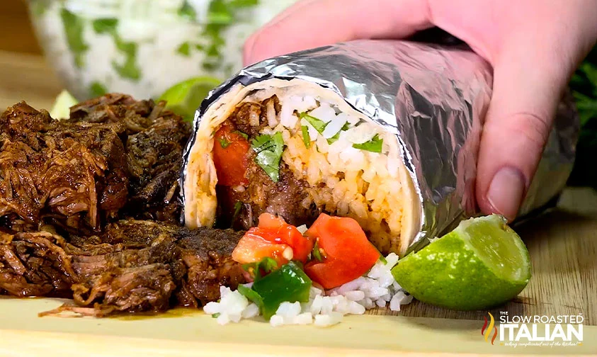 hand resting on chipotle barbacoa burrito wrapped in foil