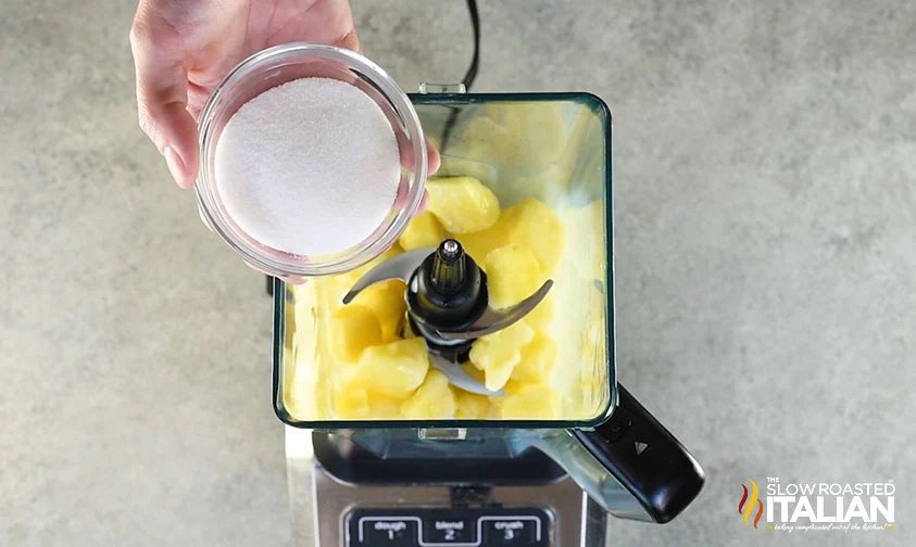 holding bowl of sugar over blender with dole whip ingredients