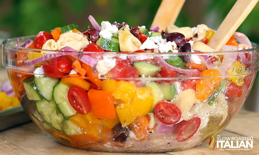 large, clear bowl of greek tortellini pasta salad topped with feta cheese