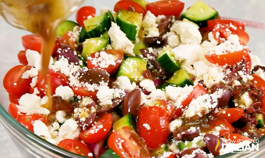 pouring homemade dressing over greek tortellini pasta salad