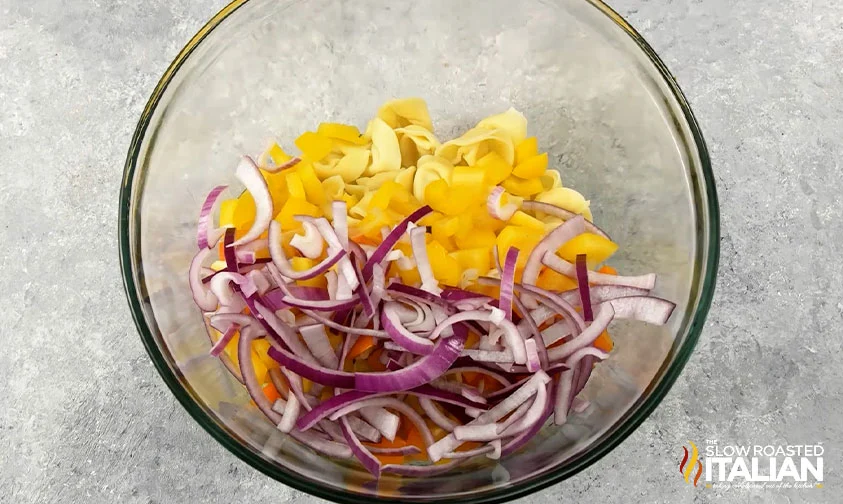 tortellini, sliced red onion, and chopped yellow and orange bell peppers in a bowl