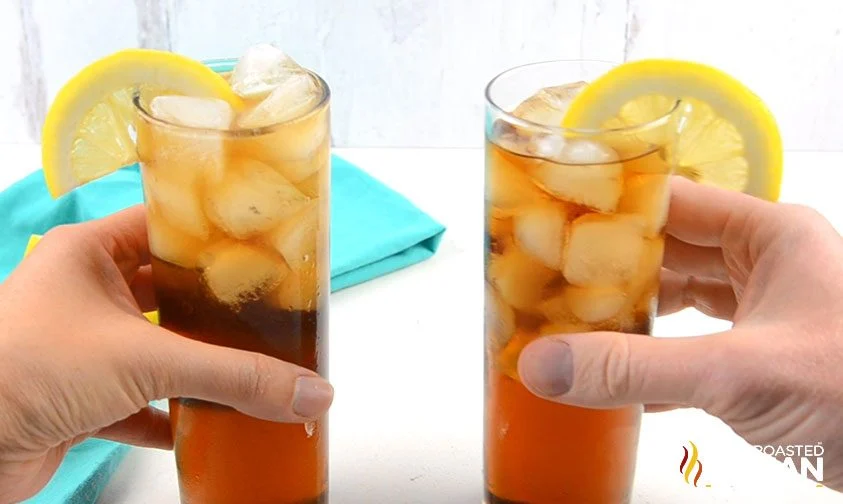 holding two long island iced teas in tall glasses with lemon slices