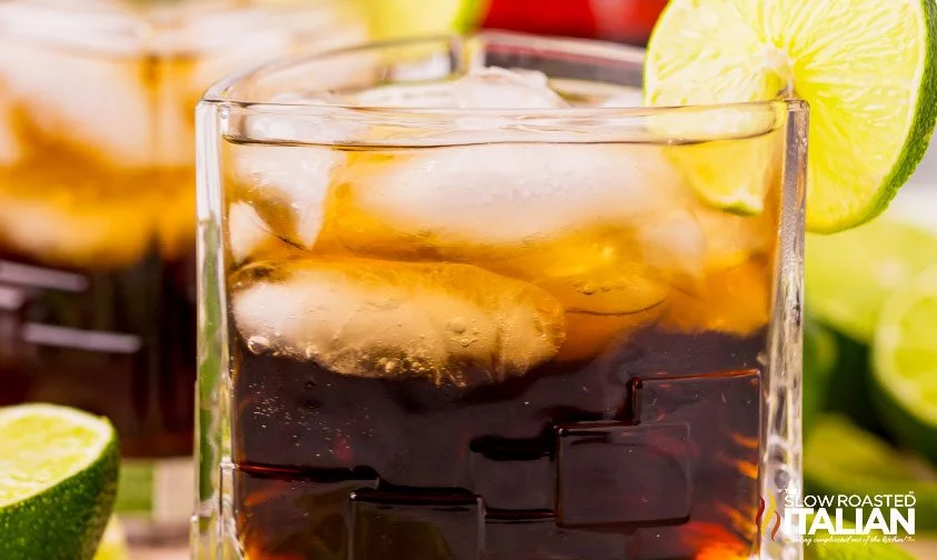 closeup: rum and coke cocktail in a triangular glass with lime garnish