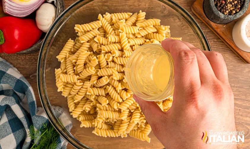 adding pickle juice to cooked pasta in a mixing bowl