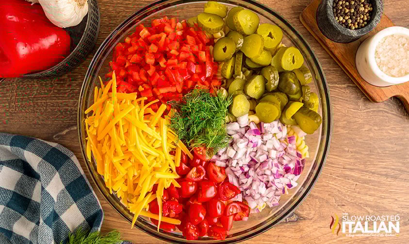 adding sliced vegetables to pasta in a large mixing bowl