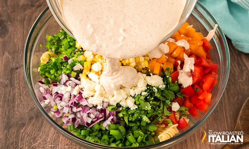 adding dressing to mixing bowl full of mexican pasta salad ingredients