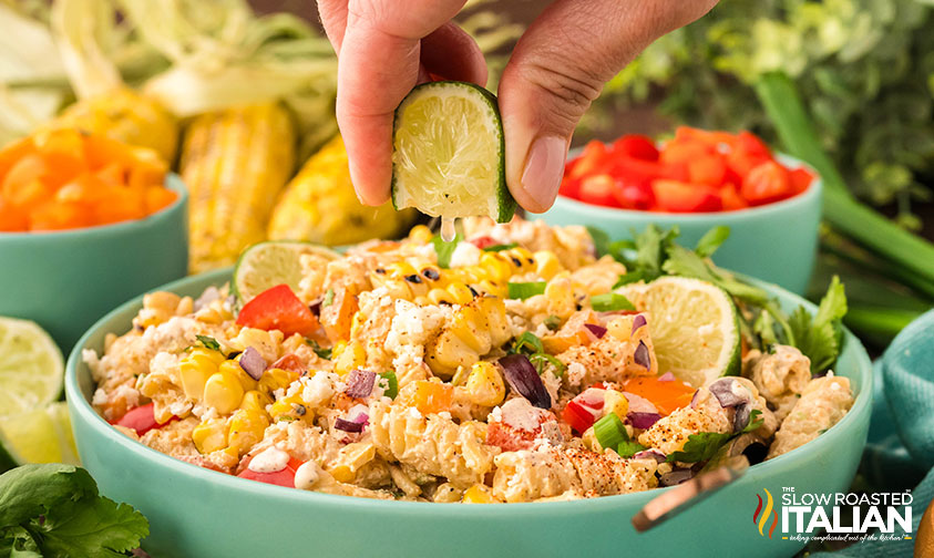 squeezing lime on a bowl of mexcian street corn pasta salad