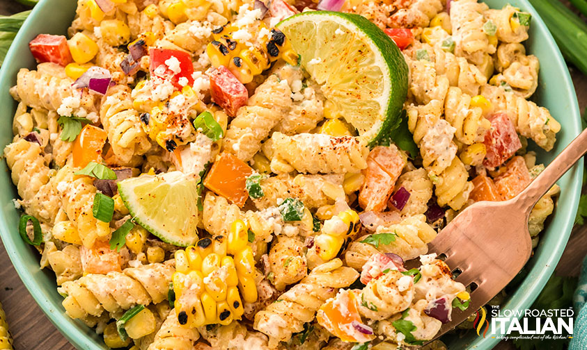 closeup of a bowl of mexican street corn pasta salad with lime wedges