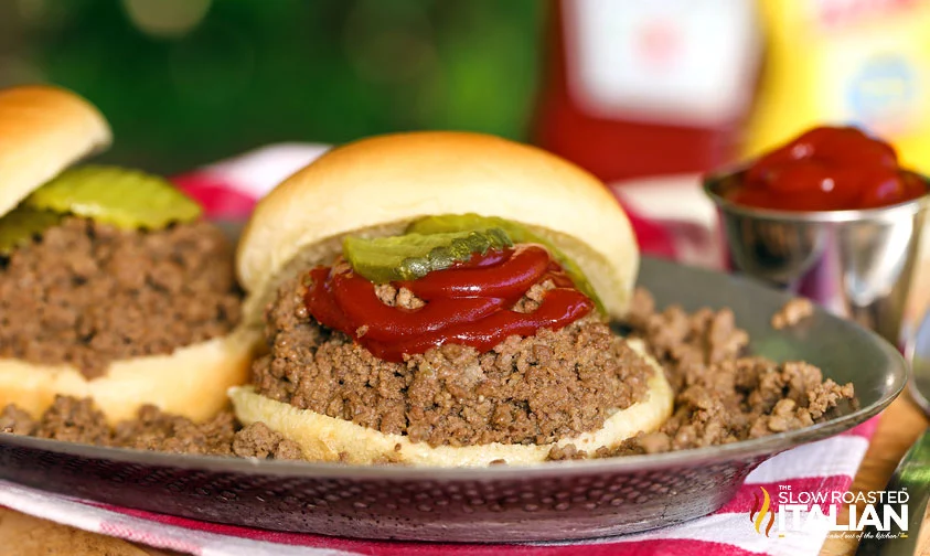 2 maid rite loose meat sandwiches on serving tray with ketchup and pickle chips