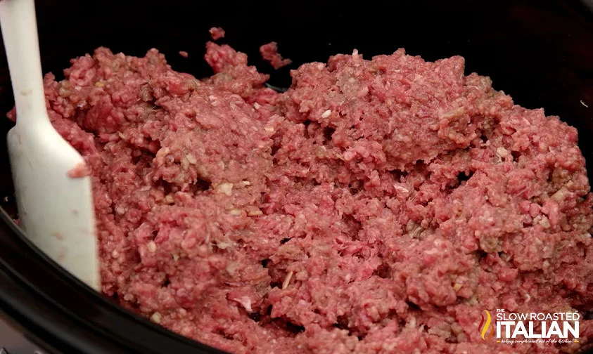stirring ground beef in crockpot with spatula