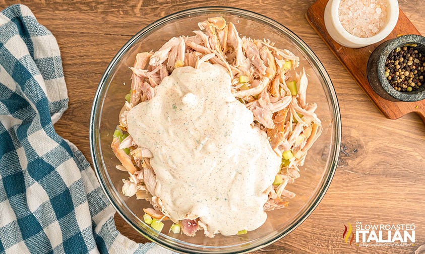 adding dressing to shredded chicken and veggies in a large mixing bowl