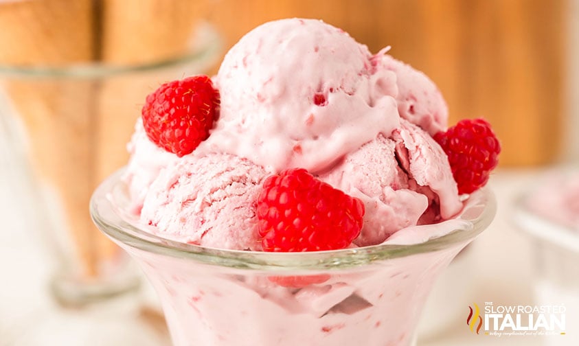 scoops of no churn raspberry ice cream in a glass bowl with fresh raspberries