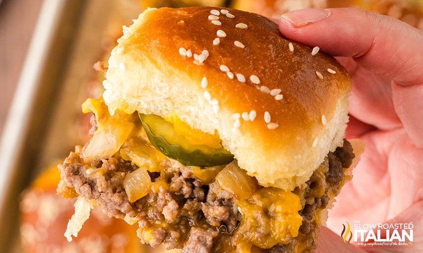 closeup of a hand holding a sheet pan cheeseburger slider