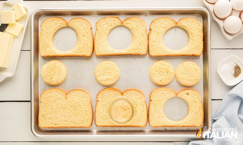 slices of bread with holes cut out of the center on a baking sheet