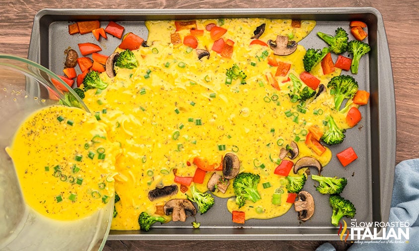 pouring egg mixture over roasted vegetables on a sheet pan