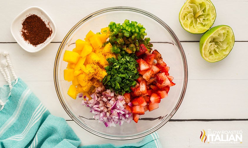 adding sliced mango, strawberries, and herbs to large mixing bowl