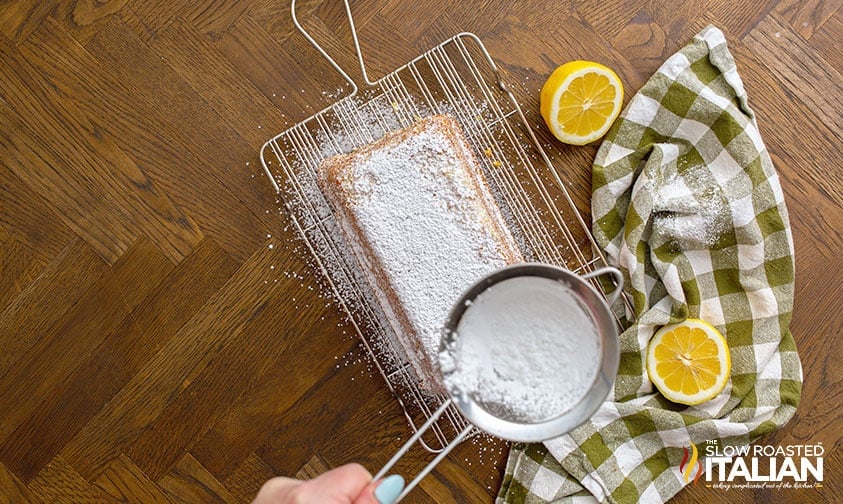 dusting powdered sugar over lemon pound cake loaf