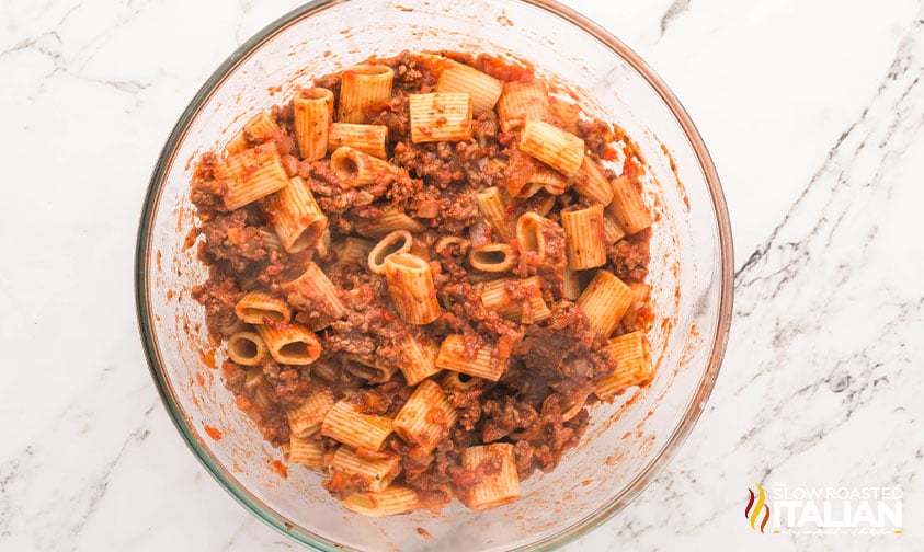 cooked pasta added to bolognese sauce in a mixing bowl