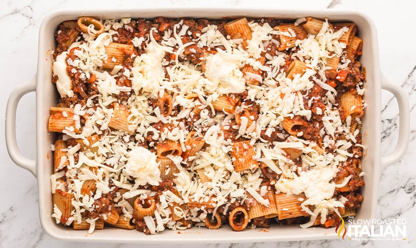 pasta bolognese added to baking dish with shredded cheese on top