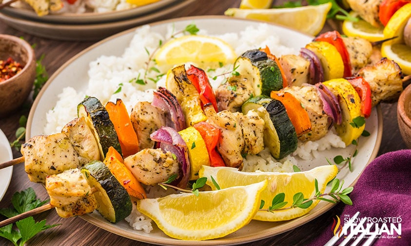 sheet pan chicken and vegetable skewers on a plate with rice and lemon wedges