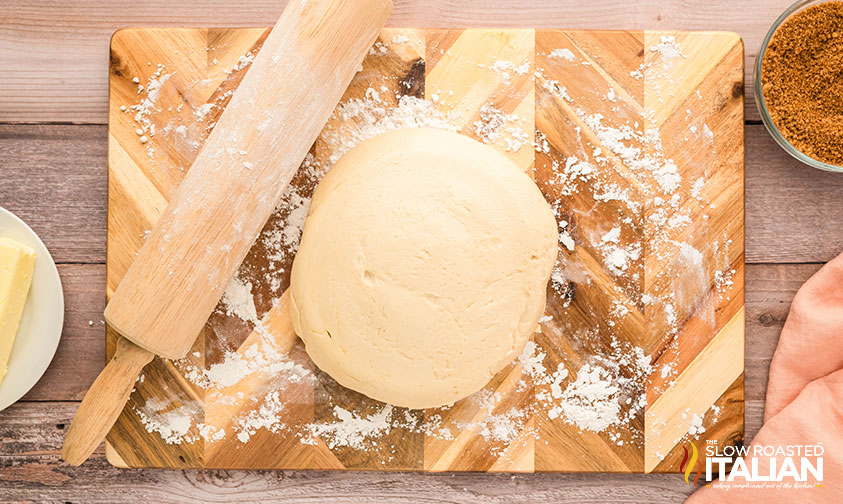rested cinnamon roll dough on a cutting board with rolling pin