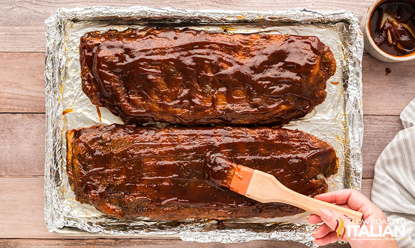 brushing baked sheet pan ribs with barbecue sauce