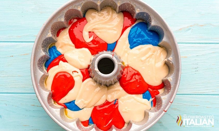 red white and blue cake batter swirled in a greased bundt pan