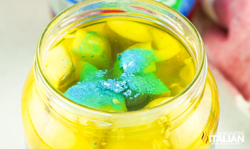 blue kool aid powder floating in a jar of pickle spears