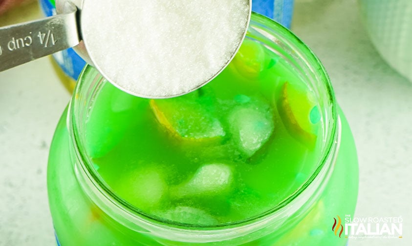 pouring sugar into a jar of green kool aid pickles