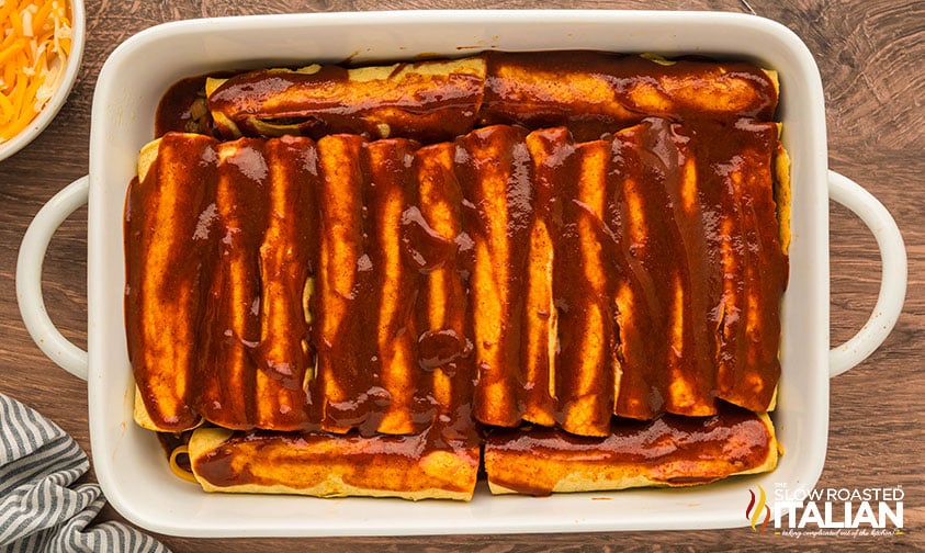 rolled beef and bean enchiladas in a baking dish smothered in red sauce