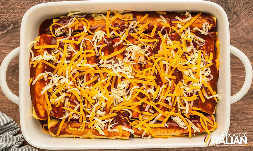 shredded cheese added to beef and bean enchiladas in a baking dish