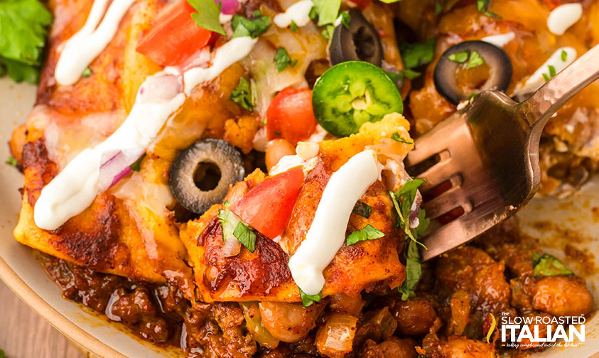 closeup of beef and bean enchiladas on a plate drizzled with sour cream