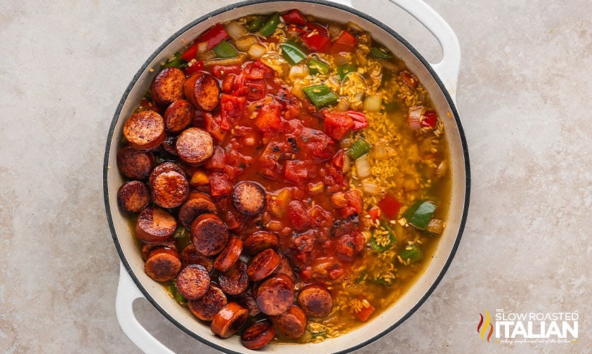 adding diced tomatoes, chicken broth and tomato paste to cajun sausage and rice