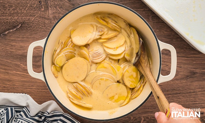 sliced potatoes added to cheese sauce in a pot for potatoes au gratin
