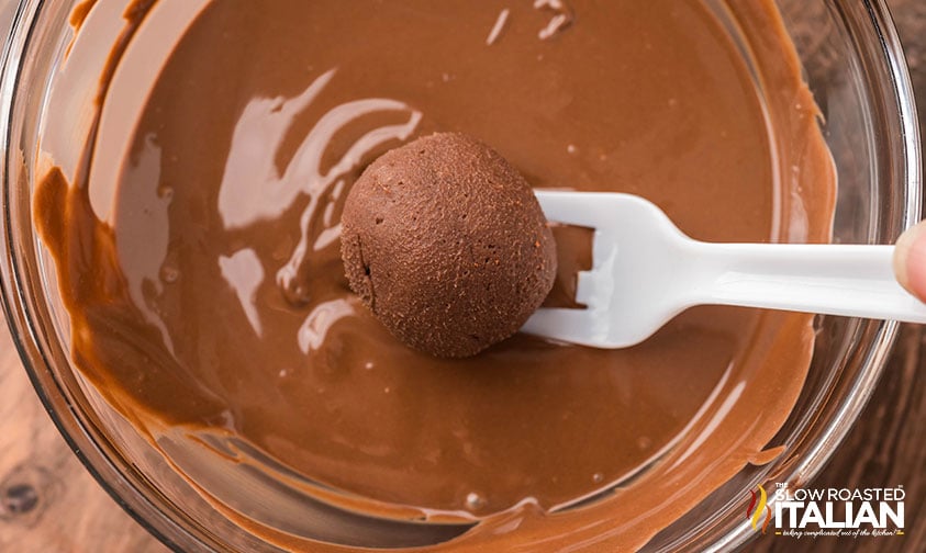 dipping chocolate truffle in a bowl of melted chocolate