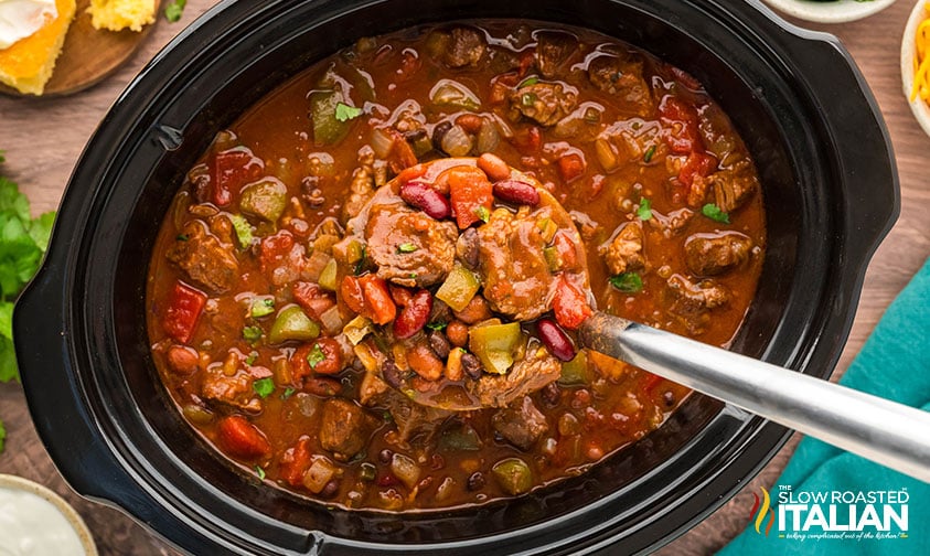 serving crockpot steak chili with a ladel