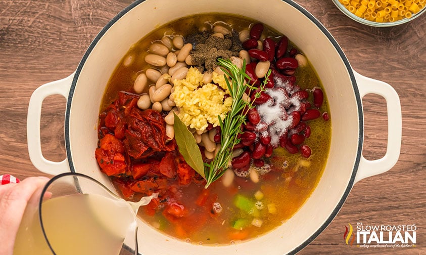 adding chicken stock, beans, and herbs to pasta fagioli in a dutch oven