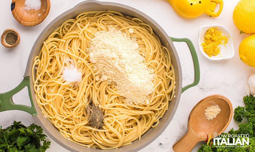 adding cheese and seasoning to cooked pasta in a skillet