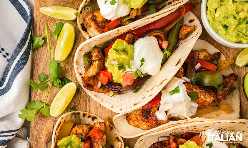 sheet pan chicken fajitas in tortillas on a serving board